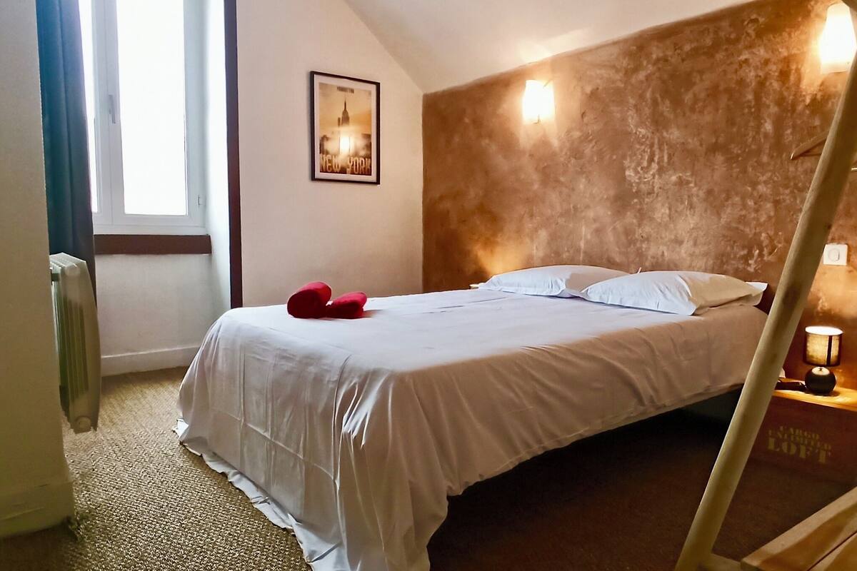 Habitación de hotel con cama, mesita de noche con lámpara, un cuadro en la pared y una ventana con cortinas.