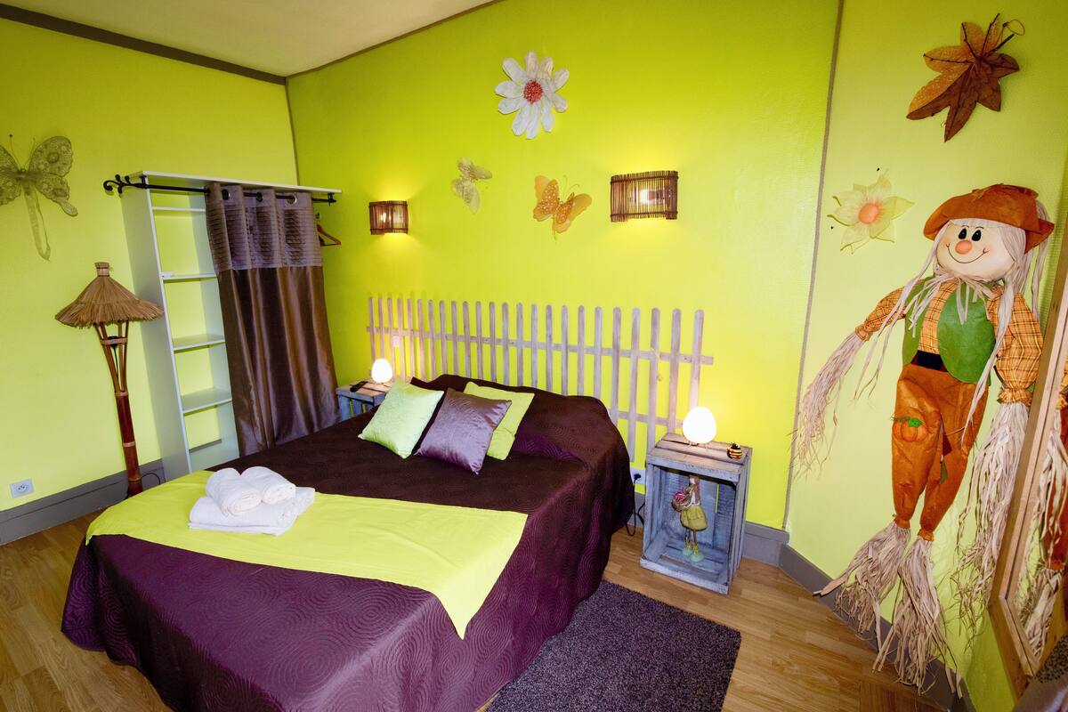 Un dormitorio con cama, almohadas, una mesita de noche, lámpara y adornos en la pared.
