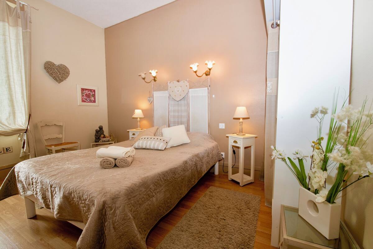 Un dormitorio ordenado con una cama grande, mesitas de noche, un espejo y un corazón decorativo en la pared.