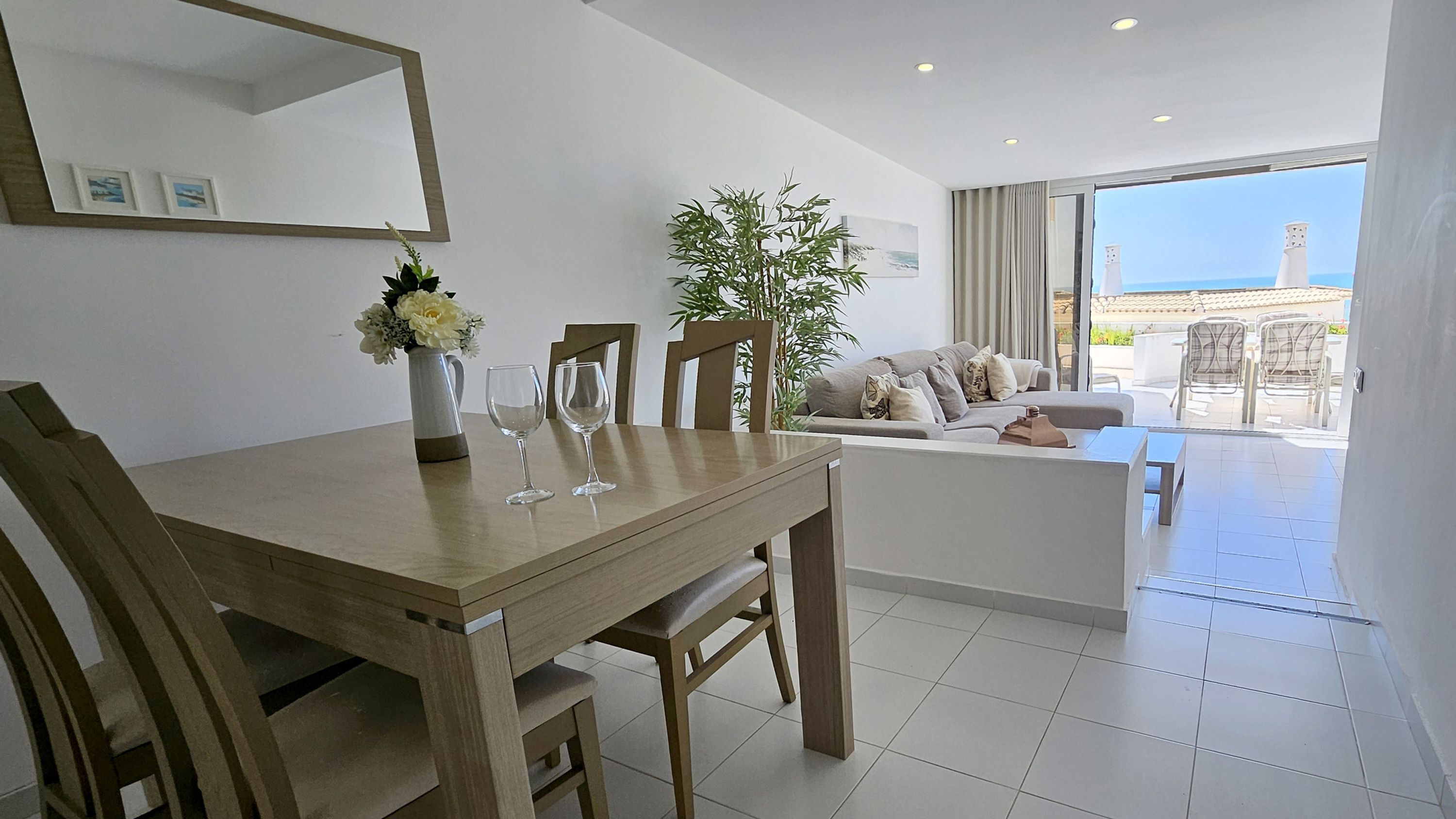 A modern living room with a dining area, large windows, and a view of the sea.
