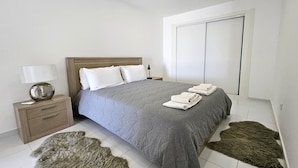 Une chambre bien rangée, avec un lit, une table de chevet, une lampe et une grande fenêtre.