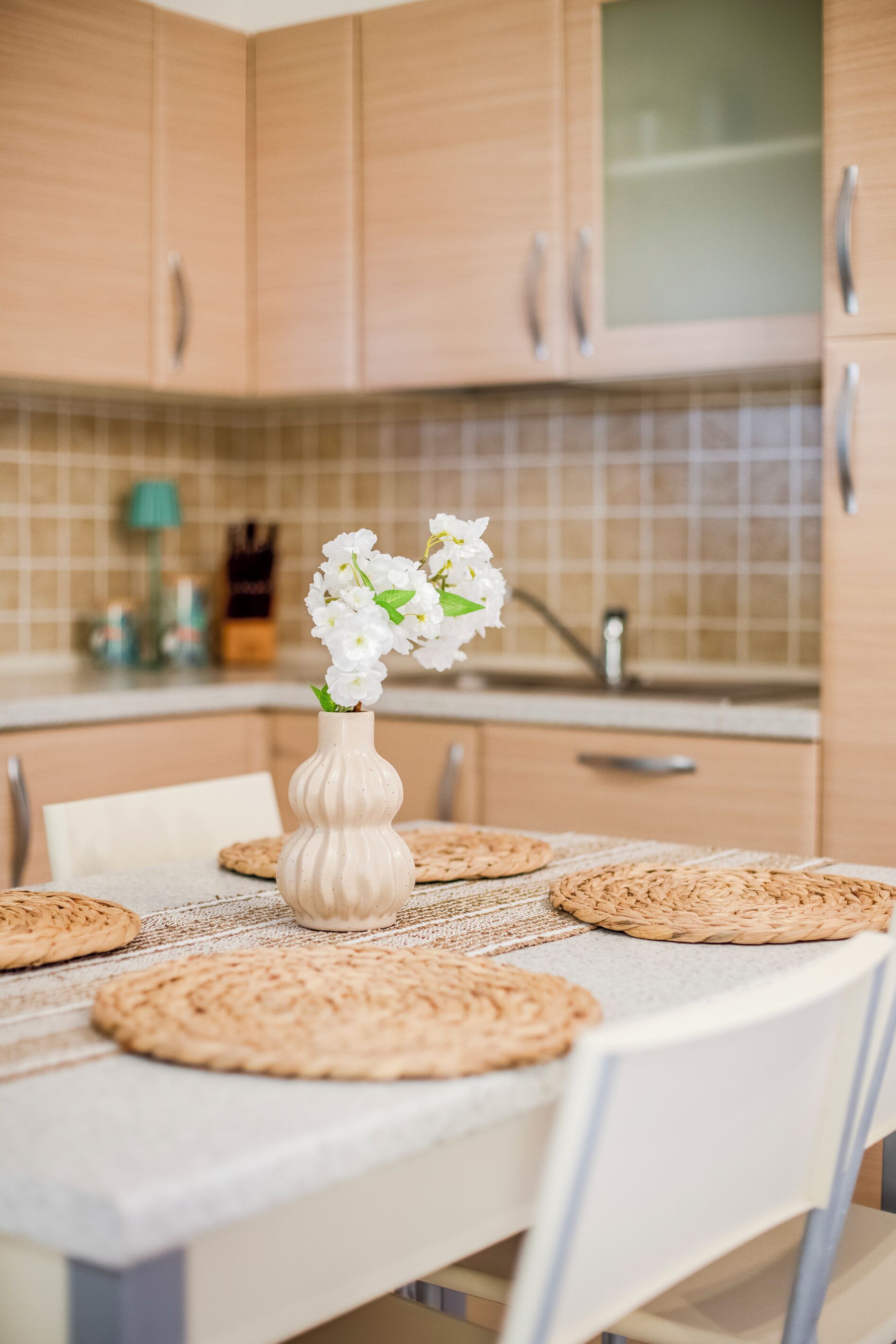 A kitchen with wooden cabinets, a white table with placemats, and a vase with flowers.