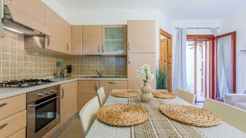A modern kitchen with wooden cabinets, a gas stove, and a dining area with a woven placemat table.