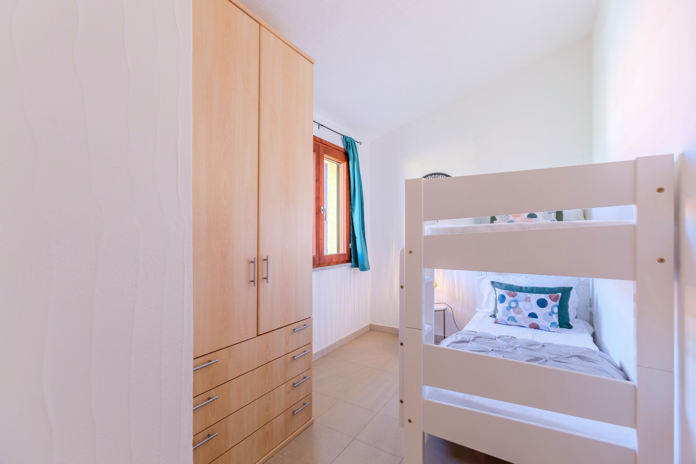 Une chambre avec un lit superposé, une armoire en bois et une fenêtre avec des rideaux.