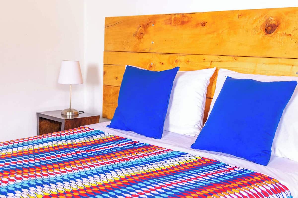 A bed with a colorful patterned bedspread, two blue pillows, and a wooden headboard.