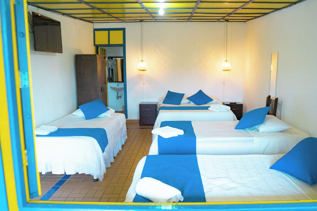 A hotel room with four single beds, a small desk, a chair, a mirror, and a sink.