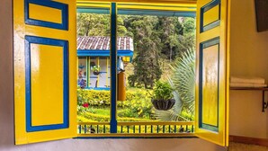 Ein Zimmer mit Fensterblick auf einen Garten, einer Holzbank und einem Klappstuhl.