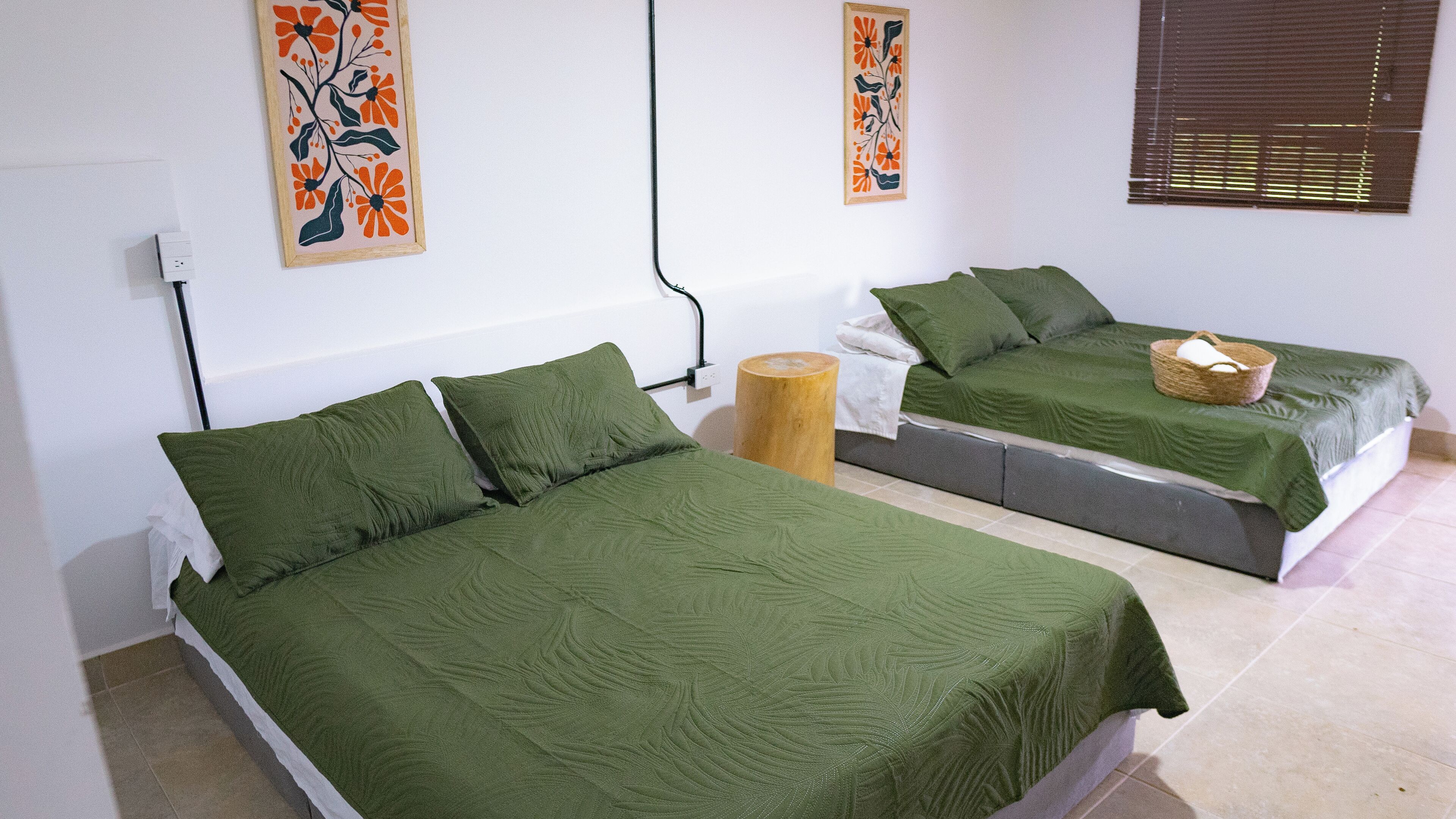 Two single beds with green bedding in a room with white walls and a wooden floor.