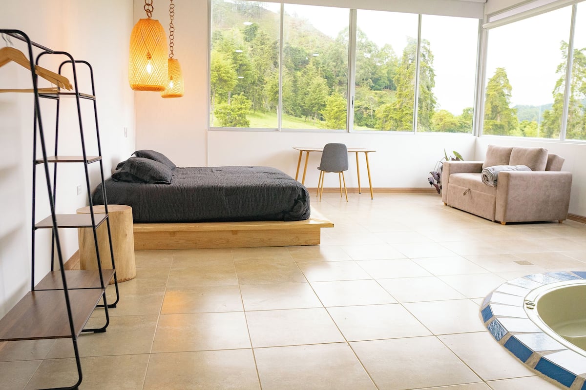 A modern bedroom with a bed, a chair, a sofa, and a view of the outdoors.