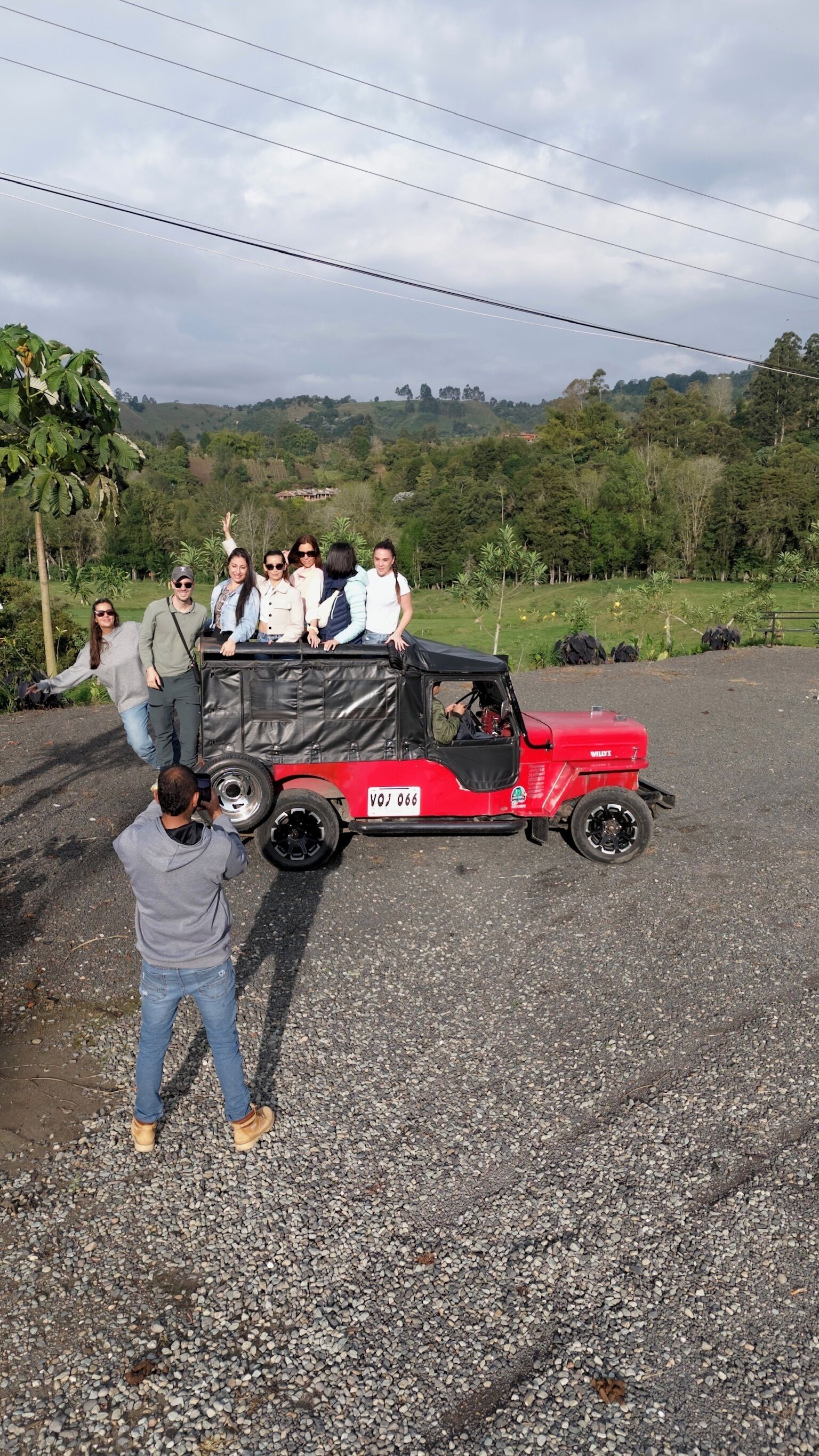 Un vehículo todoterreno rojo con pasajeros, estacionado sobre una superficie de grava con un paisaje montañoso al fondo.
