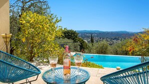 A terrace with a pool, two chairs, and a table with a bottle and glasses.