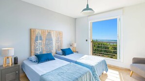 A bedroom with two beds, a large window with a view, a ceiling light, and a wall with surfboard art.