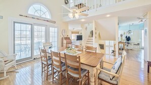 A spacious dining area with a wooden table and chairs, a large window with a view, and a staircase leading to an upper level. - Ocean View Cape May Beach Home w/ Deck | Sleeps 14 (Cape May)