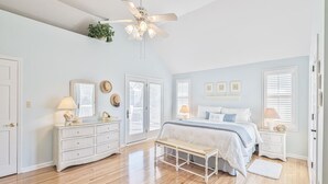 A bedroom with a bed, bedside tables, a bench, a ceiling fan, and a window with blinds. - Ocean View Cape May Beach Home w/ Deck | Sleeps 14 (Cape May)