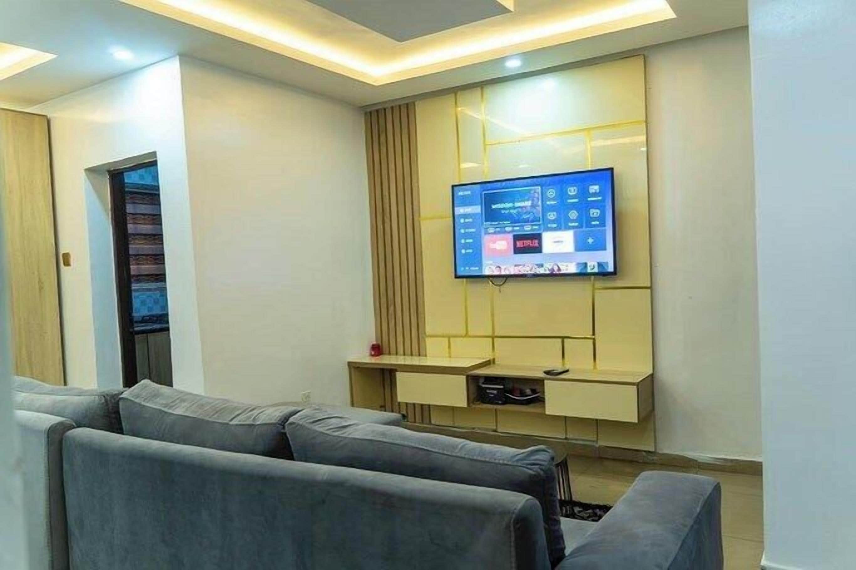 Una sala de estar moderna con un televisor de pantalla plana montado en la pared, sofás grises y una unidad de entretenimiento empotrada.