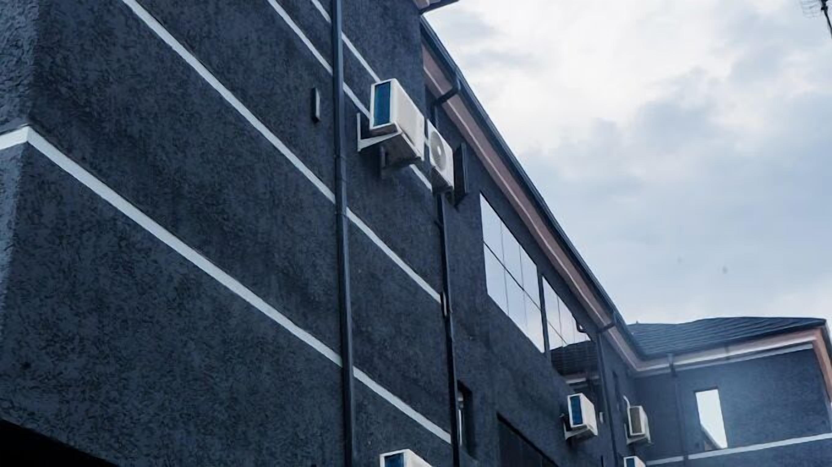 A modern building with a dark facade, large windows, and multiple air conditioning units.