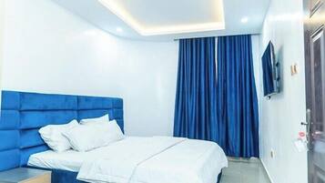 A modern hotel room with a blue headboard, white bedding, and a large window with blue curtains.