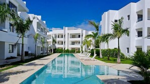 Un hotel moderno con una piscina larga, edificios blancos y palmeras.
