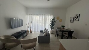 Una sala de estar moderna con un televisor de pantalla plana, un sofá, dos sillones, una mesa de comedor con sillas y una planta en maceta.