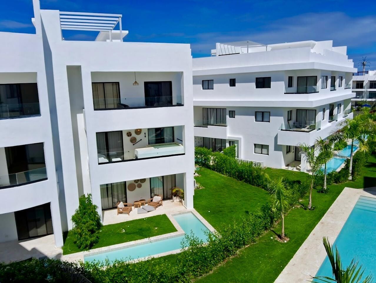 Ein modernes, mehrstöckiges Hotel mit Poolbereich, Außenbereich und üppiger Bepflanzung.