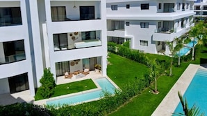 Un hotel moderno de varios pisos con piscina, zona de estar al aire libre y abundante vegetación.