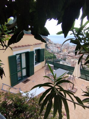 A terrace with a table and chairs, a view of the city, and a building with green shutters.