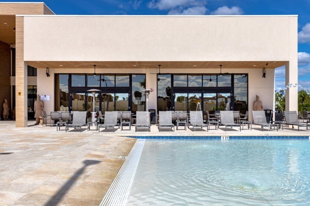 A modern building with a pool area, including lounge chairs and a clear blue pool.