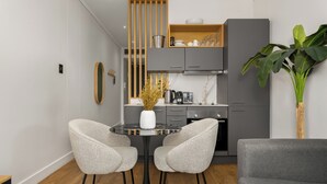 A modern kitchen with grey cabinets, a black dining table with two chairs, and a grey sofa.