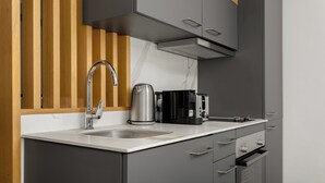 A modern kitchen with grey cabinets, a stainless steel kettle, a coffee maker, and a built-in oven.