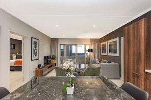A modern living room with a marble dining table, a sofa, and a TV. There is a balcony with a view. - Unwind in Luxury:2BR in Sandton w/ Private Balcony (Johannesburg)