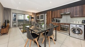 Une cuisine moderne équipée d’un four encastré, d’un lave-linge et d’un coin repas avec une table et des chaises en verre.