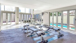 Une salle de sport équipée de matériel d’exercice, dotée de grandes fenêtres et offrant une vue sur une piscine.