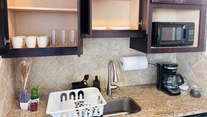 Uma cozinha com pia, cafeteira, micro-ondas e um conjunto de copos e taças nas prateleiras.