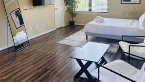 Quarto com cama, escrivaninha, cadeira, televisão, ventoinha no teto e janela com persianas.