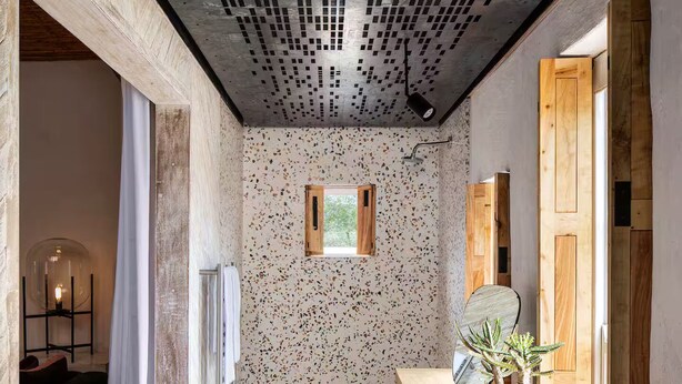 Un baño moderno con piso moteado, tocador de madera, un lavamanos grande y un techo con diseño de cuadrícula.