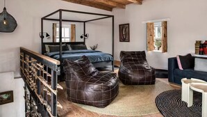 Un dormitorio con una cama con dosel, dos otomanas de cuero, una escalera de madera y vistas al exterior.