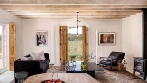 Un salón espacioso con techo de madera, una gran mesa de madera con higos, un sofá de cuero negro y un sillón de cuero negro, además de una chimenea.
