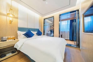 A modern hotel room with a bed, bedside table, and a sliding door leading to a balcony.