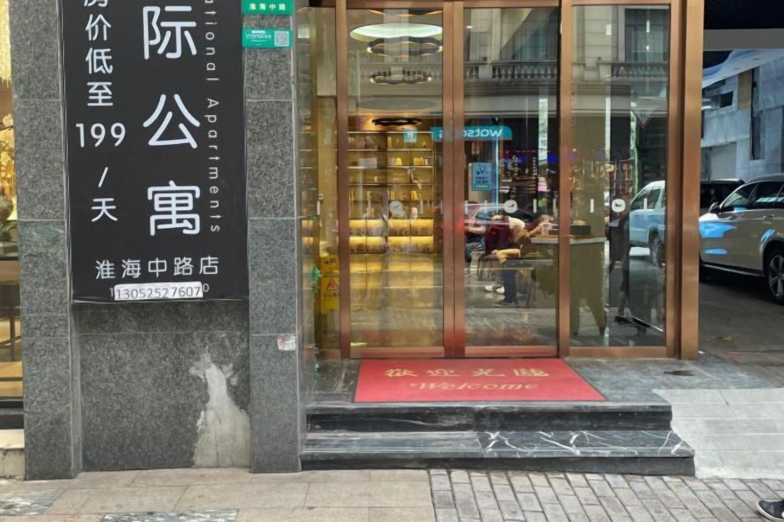 Ein Hotel Eingang mit Glastür, roher Fußmatte und einem Schild mit Zimmerinformationen.