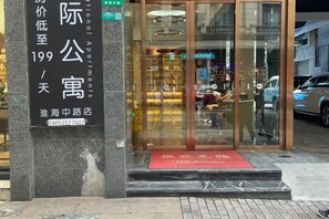 Entrada de hotel con puerta de cristal, un felpudo rojo y un cartel con información sobre las habitaciones.