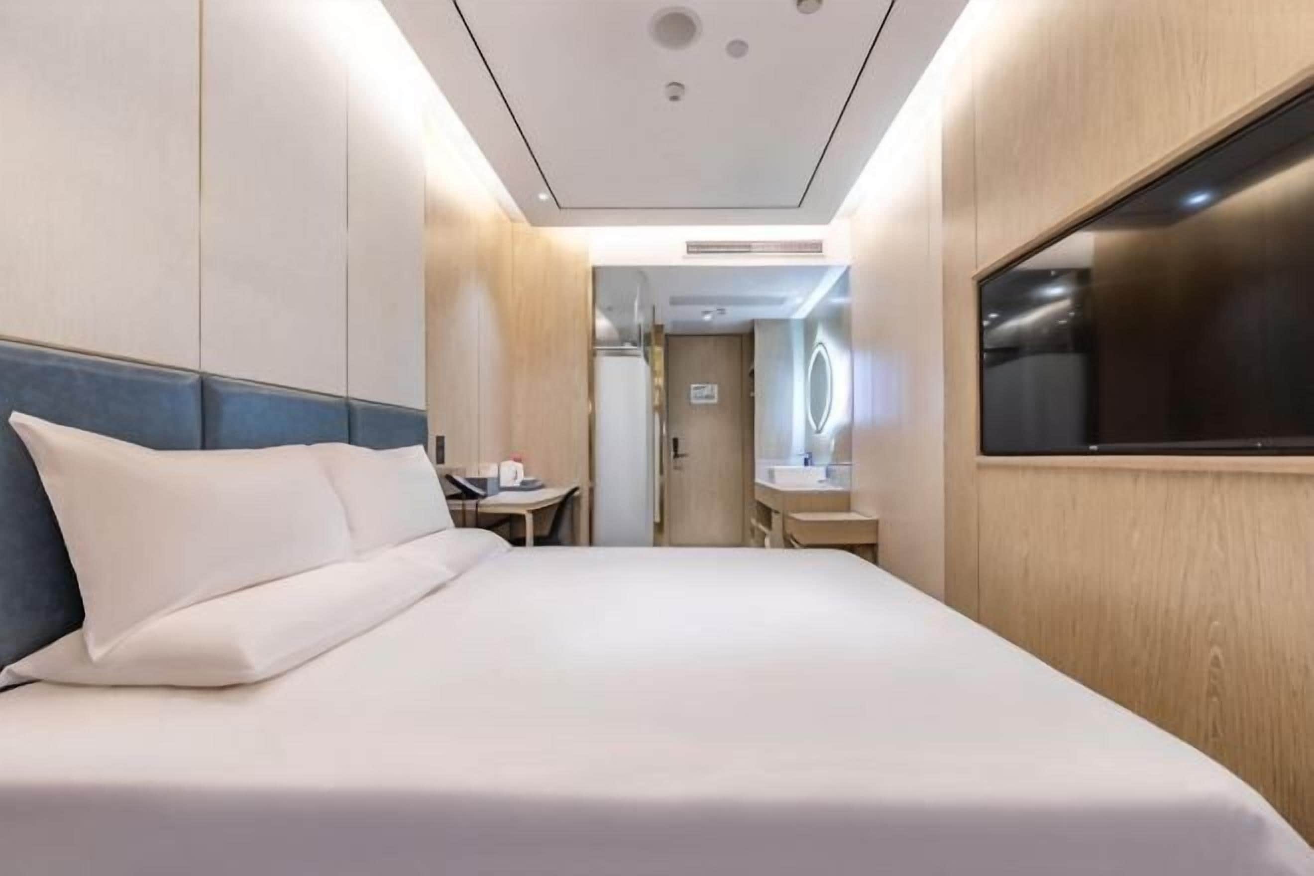 A hotel room with a bed, a desk, a mirror, and a TV.