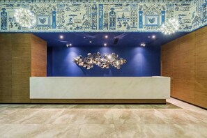 A reception area with a blue wall, a white reception desk, and a patterned ceiling. - Orange Hotel (Wuxi Oufeng Street Huishan Ancient Town Branch) (Wuxi)