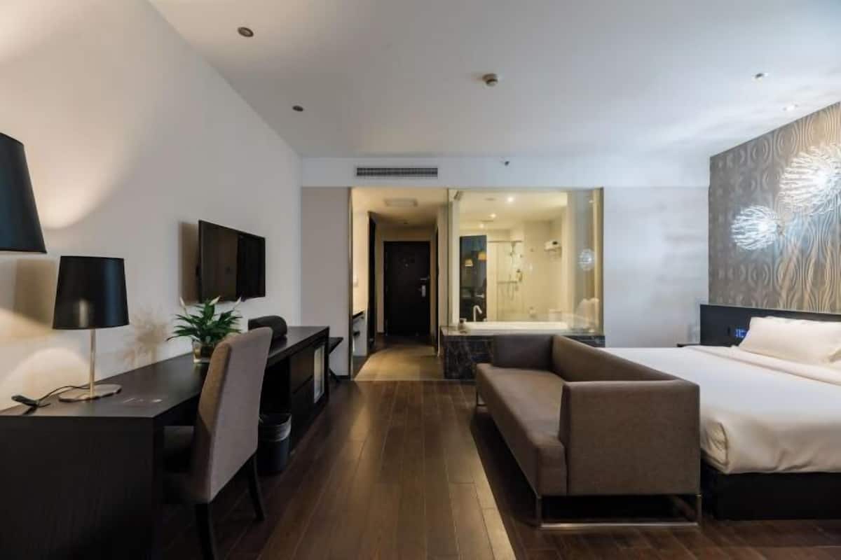 A modern hotel room with a desk, chair, sofa, and a large bed.