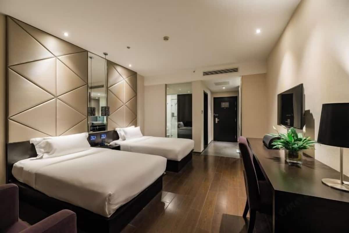 A modern hotel room with two beds, a desk, a mirror, and a television.