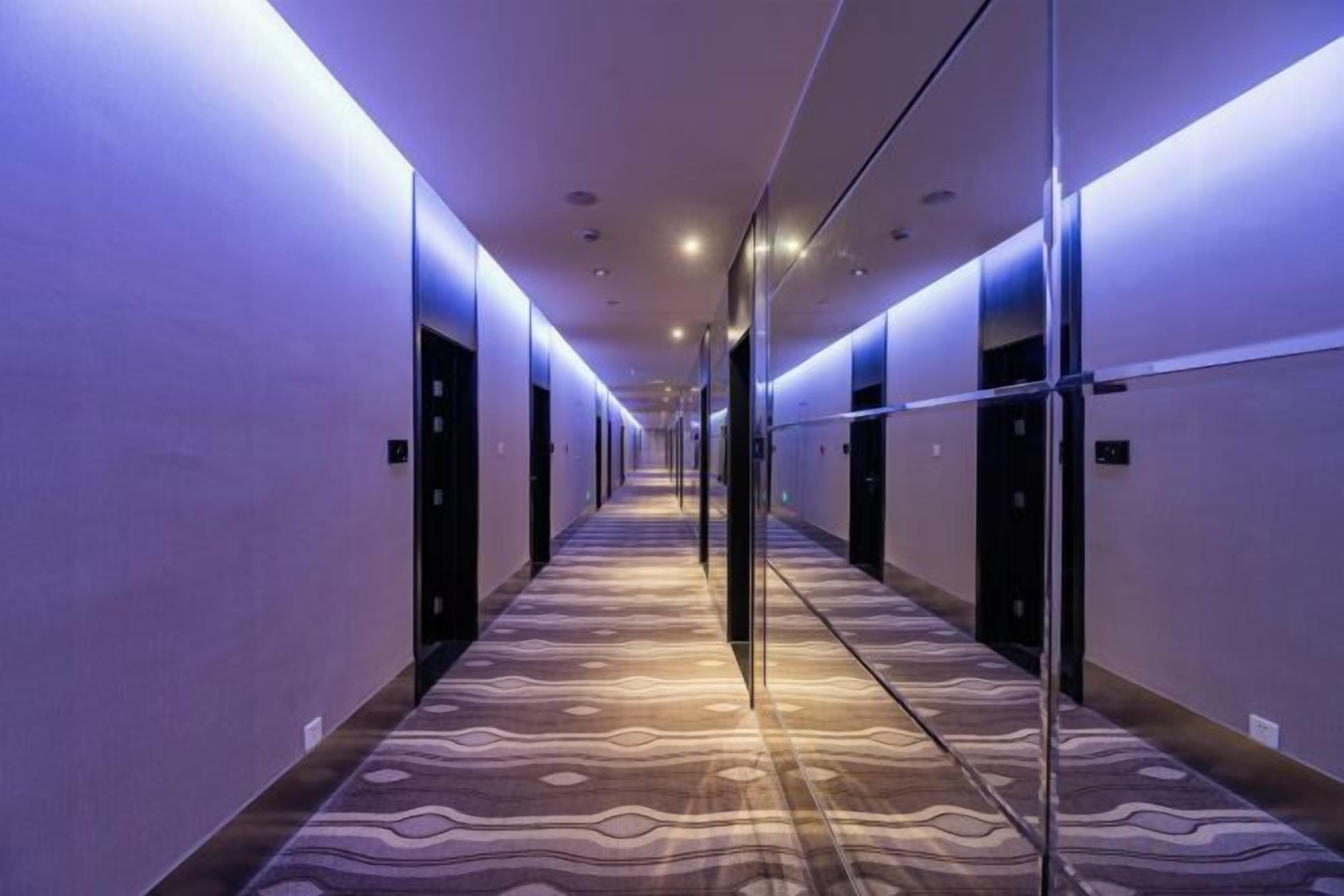 Corridoio di un hotel con tappeto a motivi, porte su entrambi i lati e una parete divisoria in vetro.