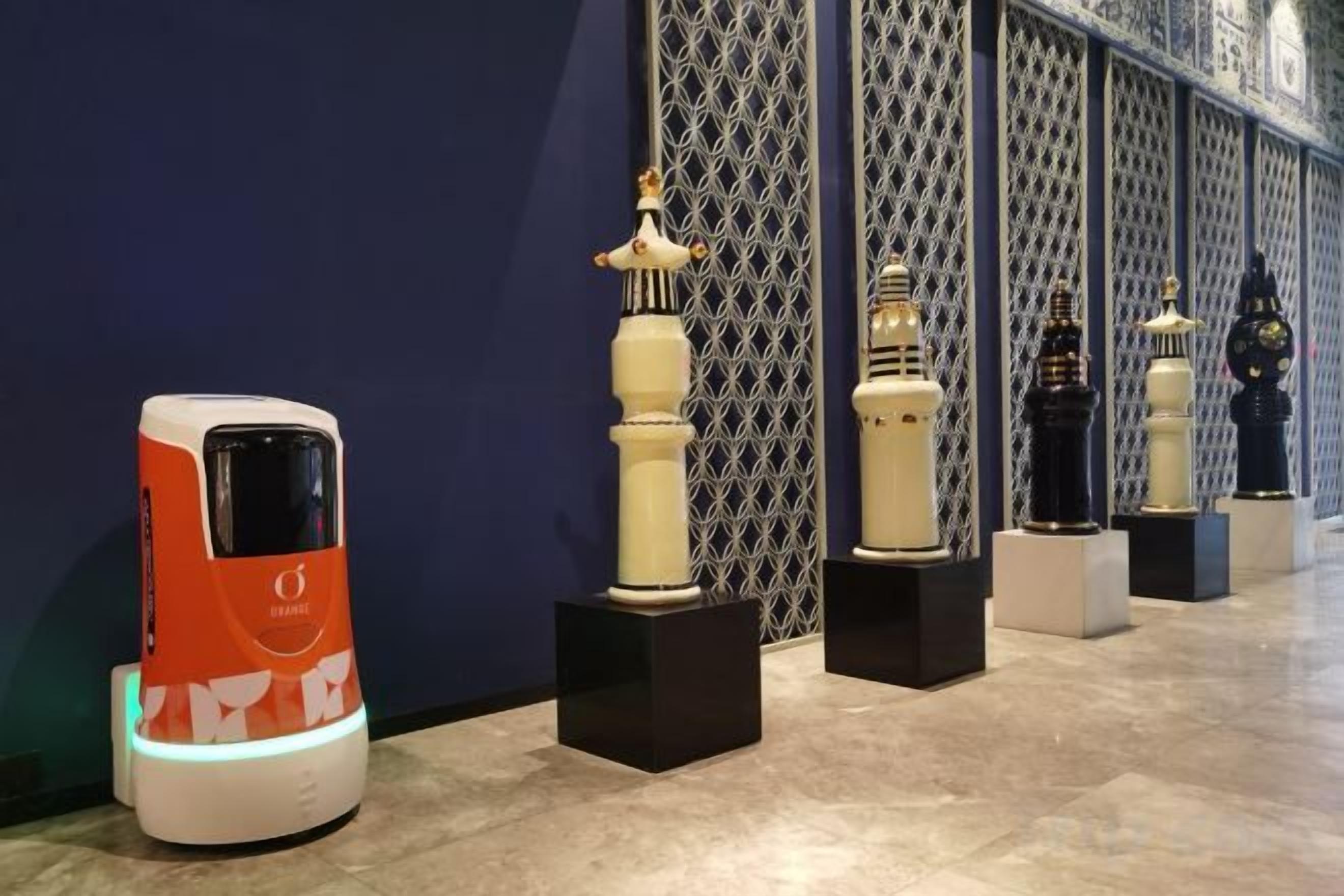 A row of objects on display against a patterned wall, with a modern vehicle-like object on the left.