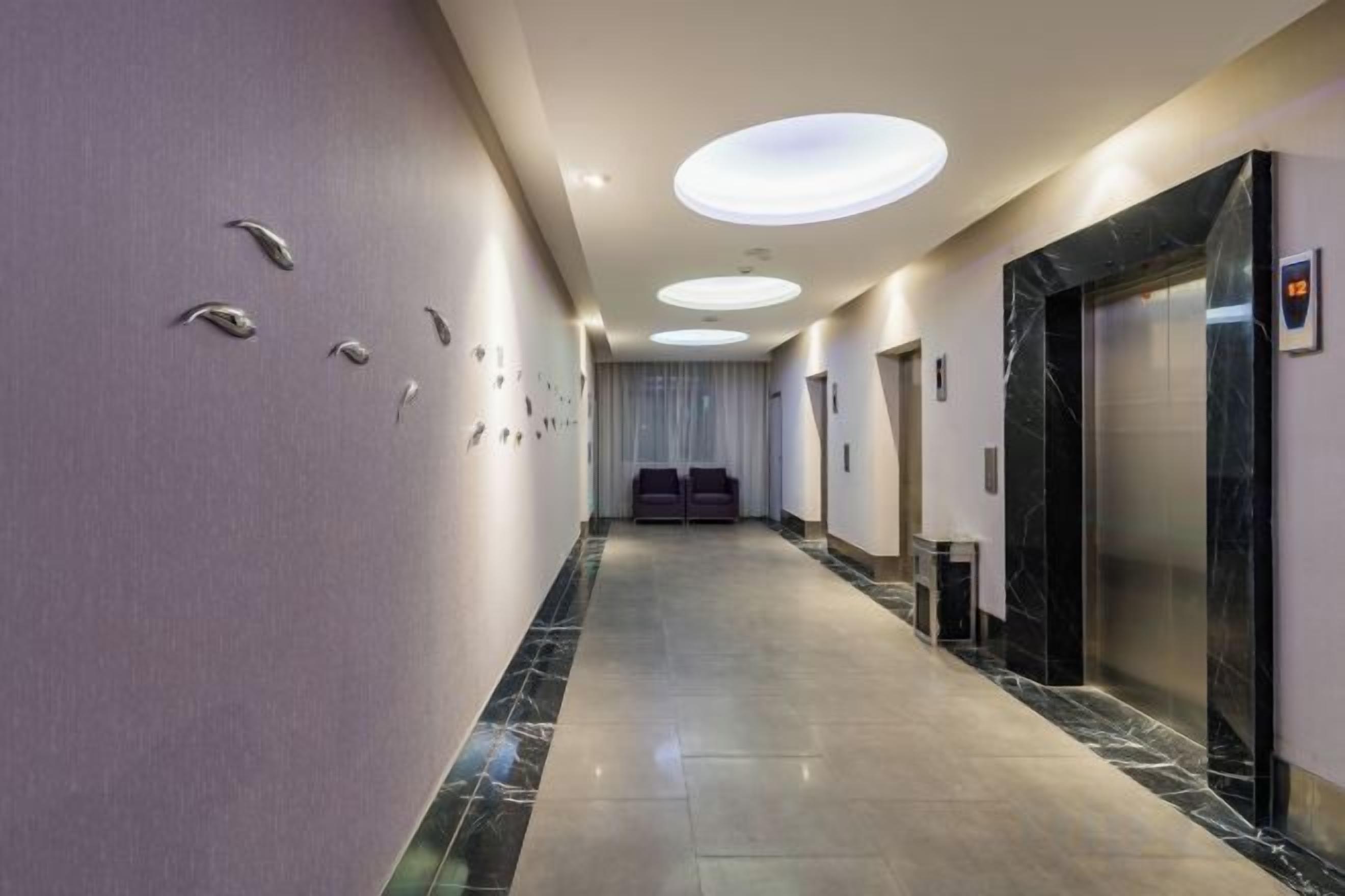 Un corridoio d'hotel con pavimento in marmo, illuminazione a incasso e una zona reception con scrivania e sedie.