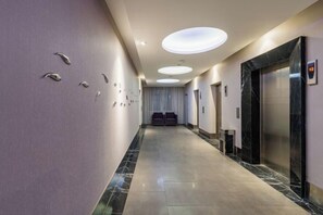 A hotel corridor with a marble floor, recessed lighting, and a reception area with a reception desk and chairs. - Orange Hotel (Wuxi Oufeng Street Huishan Ancient Town Branch) (Wuxi)