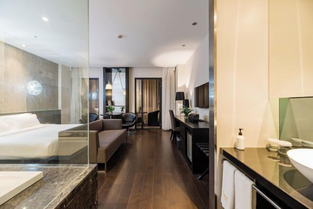 Une chambre d’hôtel moderne dotée d’un grand lit, d’un bureau, d’un canapé et d’une salle de bain avec un grand miroir et un lavabo.
