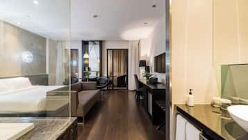A modern hotel room with a large bed, a desk, a sofa, and a bathroom with a large mirror and sink.
